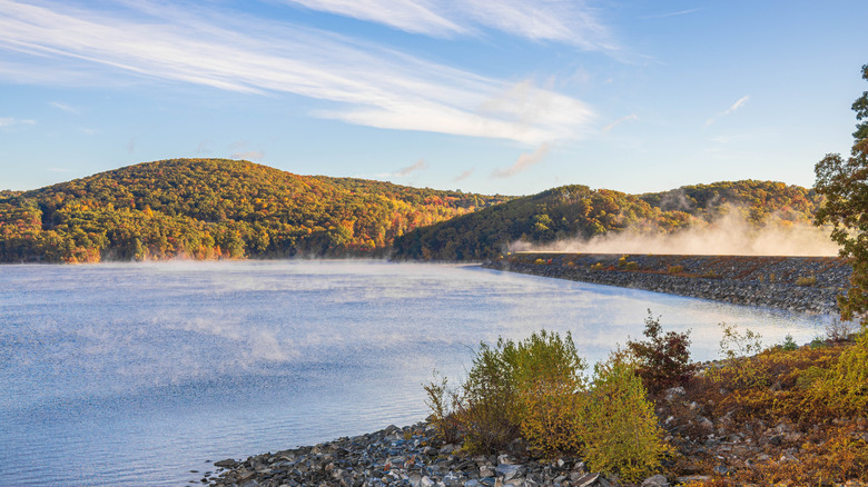 Fog rising from Quabbin Reservoir in Massachusetts with fall foliage hills in backdrop.