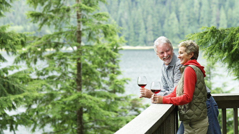 A retired couple enjoying a glass of red wine on a deck overlooking water and trees