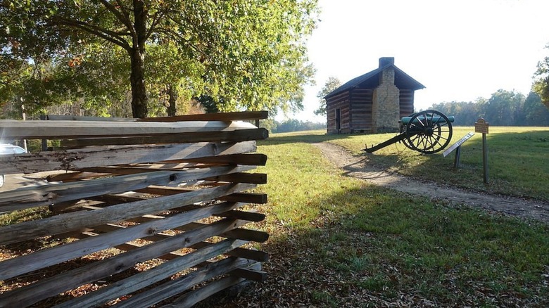A scenic trail with a fence, log cabin and antique artillery beside a trail through Chicamauga Battlefield in Catoosa County, Georgia