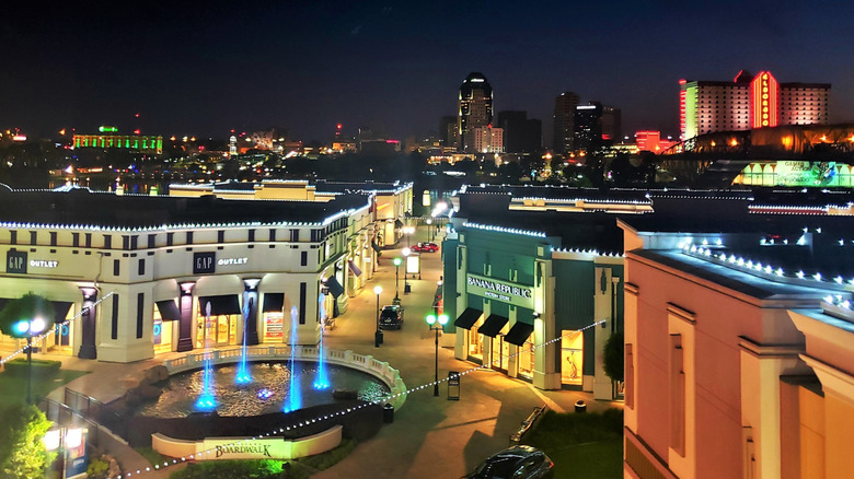 Fountains and stores at night at Louisiana Boardwalk Mall in Bossier City with Shreveport's skyline in background.