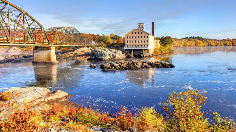 A view of the rive and bridge in Topsham, Maine, with fall foliage in the surrounding trees and a historic building on the water's edge
