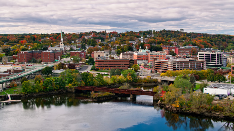 A white church spire, fall trees, and modern buildings by water in Bangor, Maine