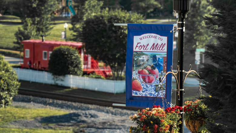 A lamp post sign "Welcome to Fort Mill" with the historic depot blurred in the background