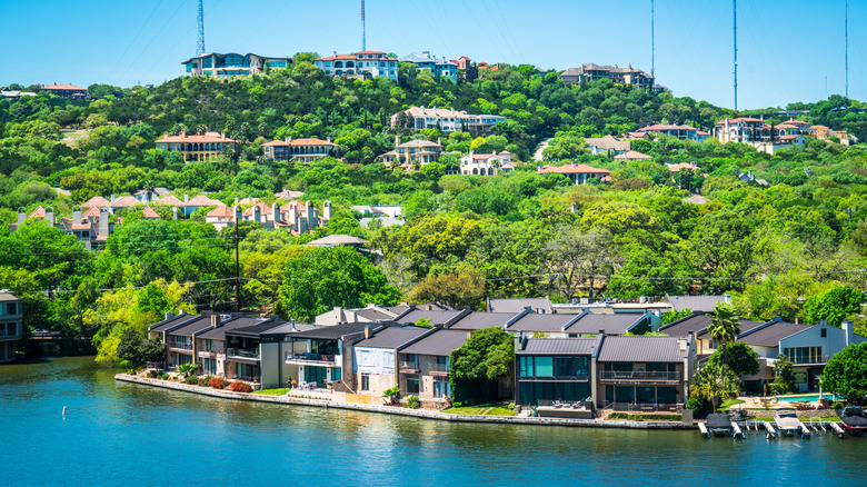 Luxurious houses along the river and on the hills surrounded by lush trees on a bright, clear day in West Lake Hills, TX