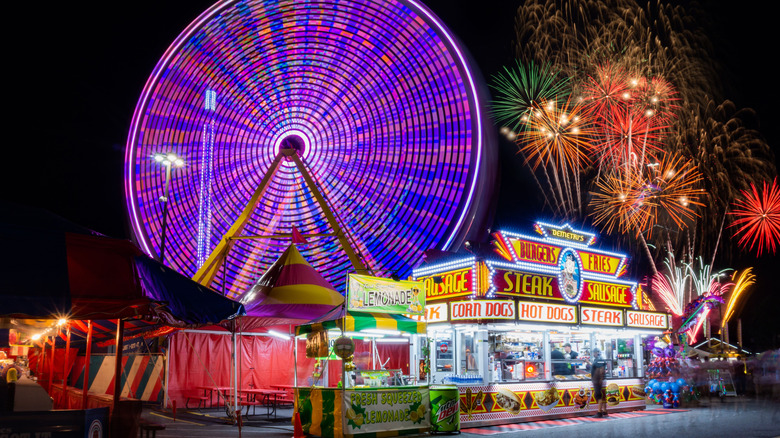 Nighttime shot of the Delaware State Fair with a Ferris wheel in motion and a carnival food stand serving steak and hot dogs