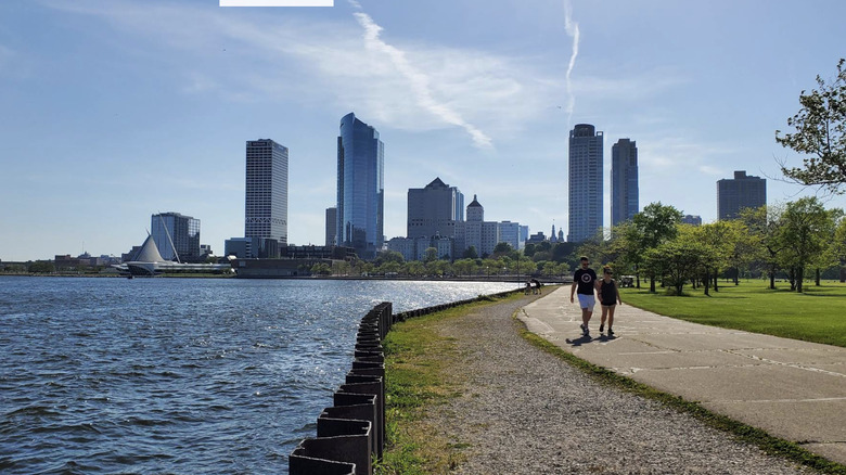 People walking on a sidewalk between Lake Michigan and a green park pace in Milwaukee, Milwaukee County, WI