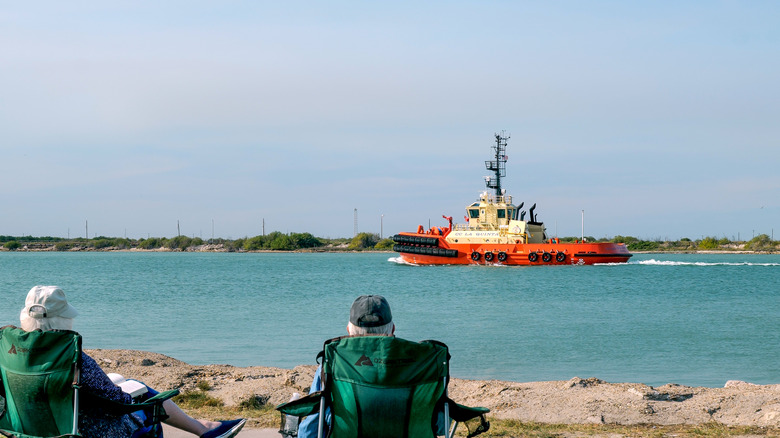 Two seniors watch a tug boat chug past the waterfront in Corpus Christi, Texas on a sunny day