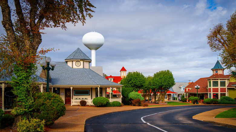 Buildings, trees and bushes lining an empty road with a water tower on a cloudy day in downtown Osage Beach, Missouri
