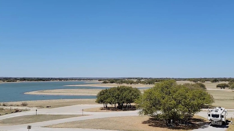 Scenic aerial view of Hords Creek Lake located in Coleman County, Texas, featuring calm blue waters, grassy shorelines, scattered trees, and an RV parked at a campsite