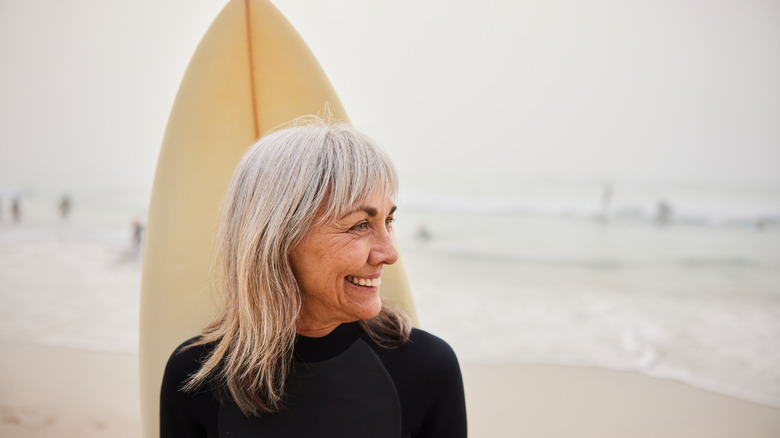 Gray-haired woman with her surfboard on the beach