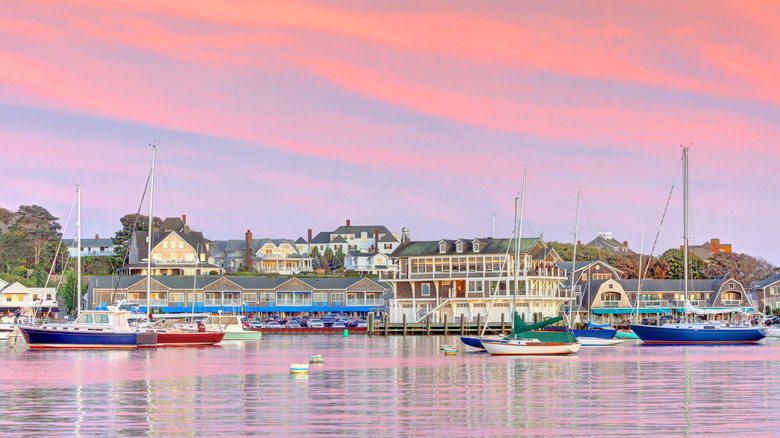 View from the water of coastal residences lining the shore around sunset, with colorful sailboats docked in the waters off of Watch Hill, Westerly, Rhode Island