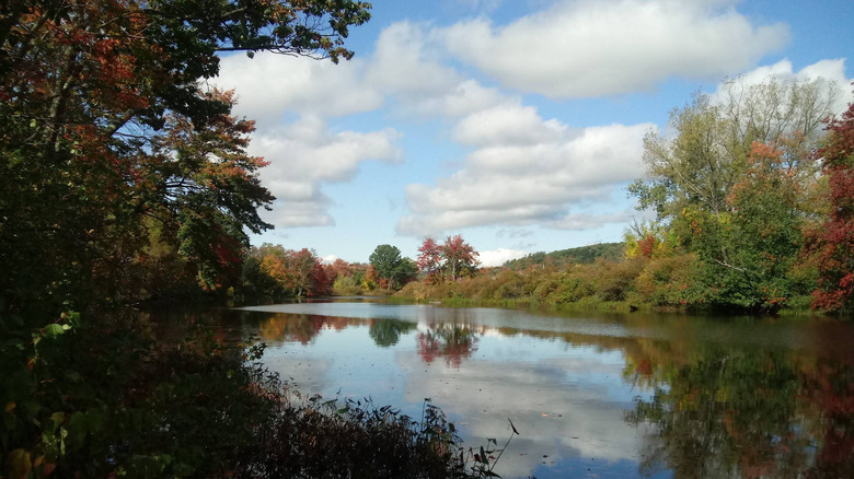 View of Millers River at Orange, Massachusetts with a cloudy blue sky, fall colors, and a glassy surface