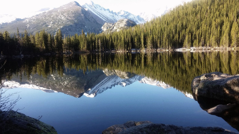 The still blue water of Bear Lake against the backdrop of forested hills and mountains in northern Utah