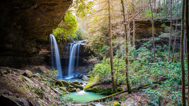 Views of a double waterfall cascading over a rocky overhang inside a wooded area at Daniel Boone National Forest in Kentucky.