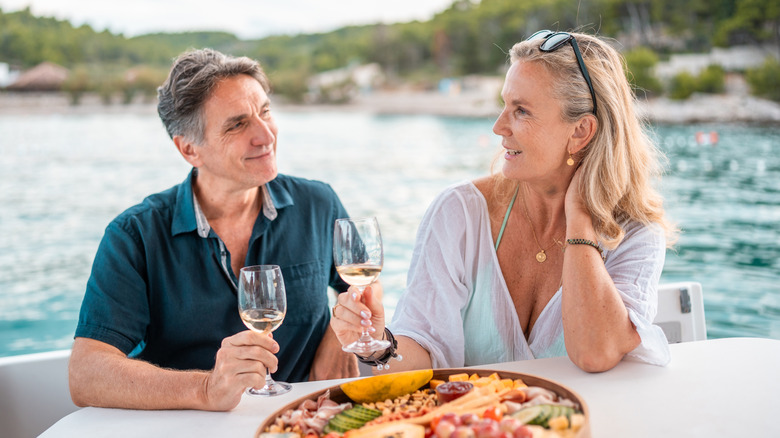 A smiling retiree couple sipping white wine and having a meal on the waterfront in Croatia
