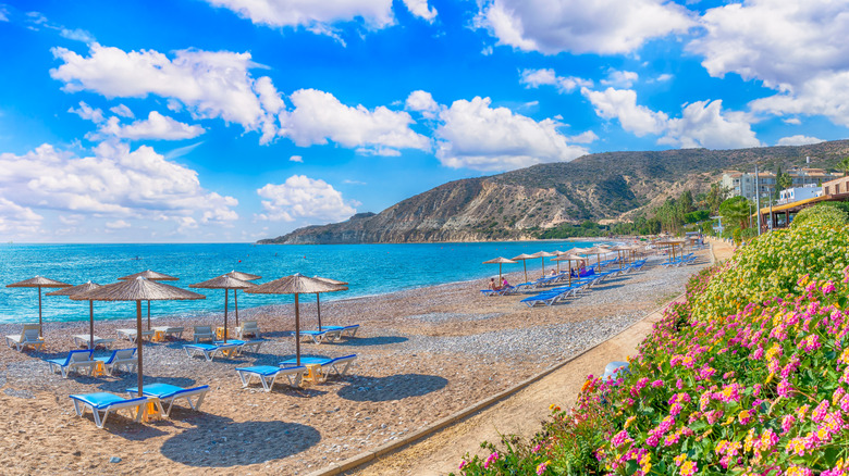 Chaise lounges and umbrellas line a sandy beach with deep clue waters in Limassol
