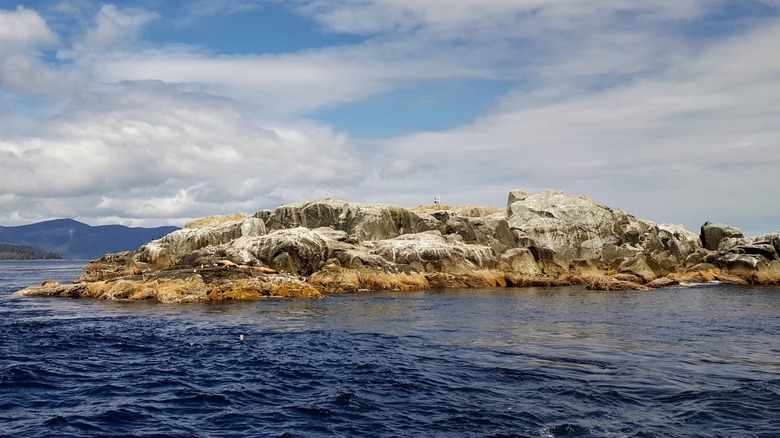 A rocky islet surrounded by deep blue water and skies at Gwaii Haanas National Park Preserve.