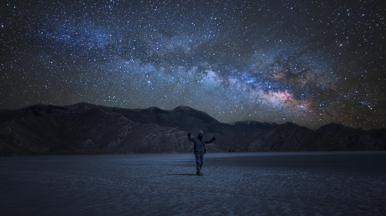 a man enjoys himself on Pangong Lake's frozen surface with the Milky Way visible in the sky at night