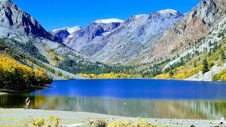 Two people fish at the edge of Lundy Lake with massive mountains surrounding it.