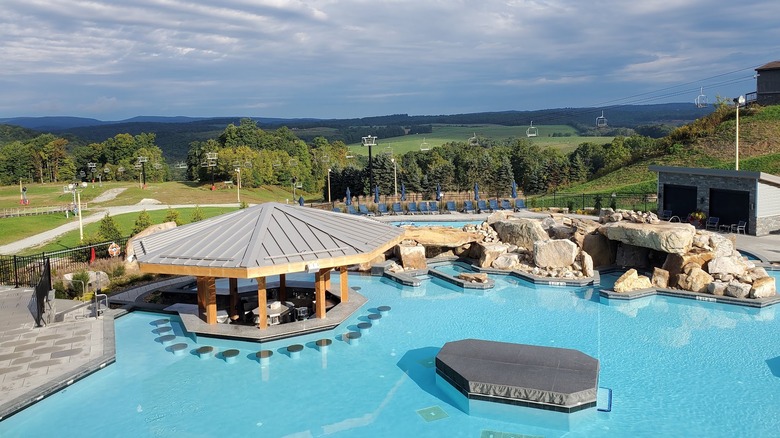 View from Nemacolin Resort, with a pool with a swim-up bar in the foreground and tree-covered hills in the background,