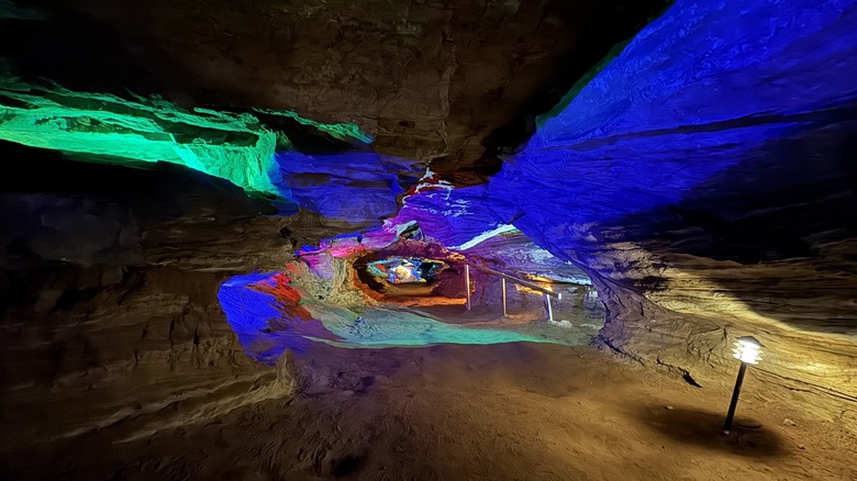 Interior of the Laurel Caverns, with green, blue, and red-lit rock passages, and a short black light post and wooden railing along the right