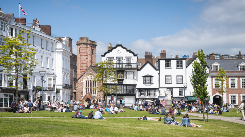 People lounging on the grass against the backdrop of traditional Exeter buildings
