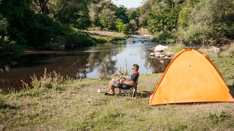 A man sitting near a tent camp besides a gentle river