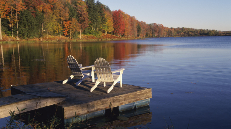 Two Adirondack chairs on a dock overlooking a lake with fall foliage in the Pocono Mountains in Pennsylvania