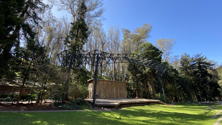 Outdoor performance stage with a curved metal canopy surrounded by tall trees at Sigmund Stern Recreation Grove, California