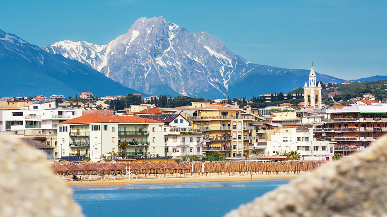 The Pescara seafront with palapas, buildings, and rugged mountains in the background