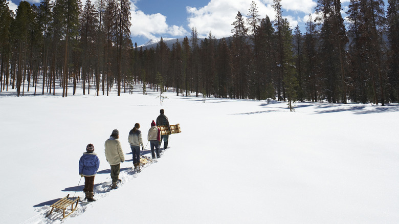 Sledders dragging their sleds in a snowy landscape in Colorado