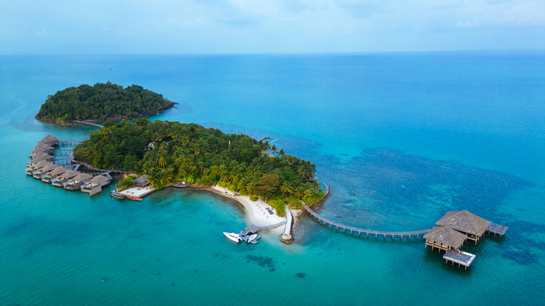 Top view of a secluded island on blue waters with stilted huts and boats docked along a pier
