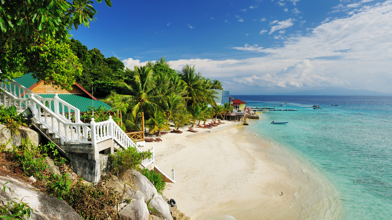 One of the sandy beaches surrounded by lush foliage on a bright, cloudy day in The Perhentian Islands, Malaysia