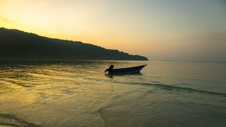Sunrise on a beach in the Perhentian Islands with a boat and mountains in the background