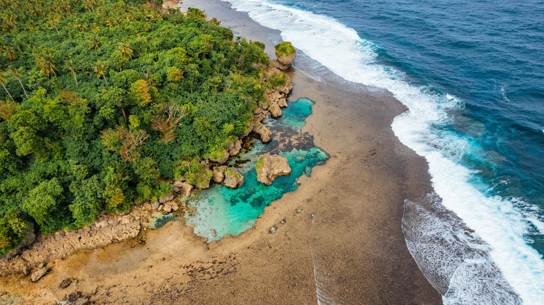 Aerial view of tidepools at Surigao City's Magpupungko Beach with surf breaking and green trees bordering one side, Philippines
