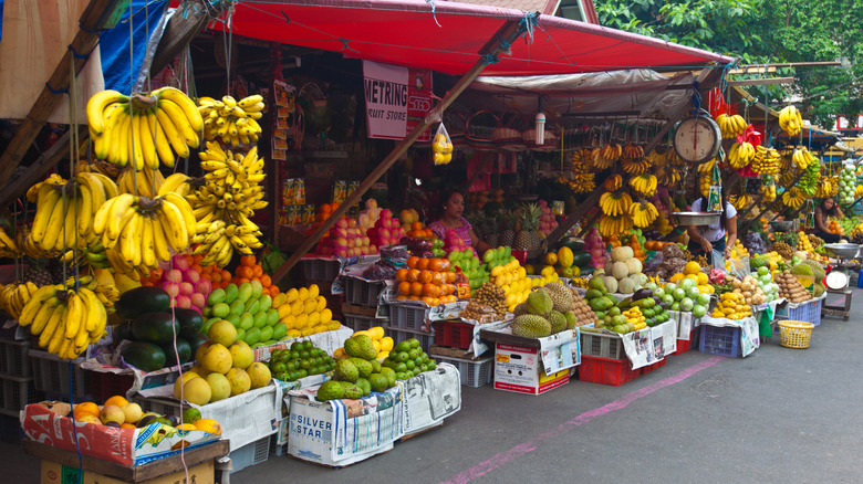 Outdoor fruit stands with displays of bananas, pomelos, mangoes, and jackfruit