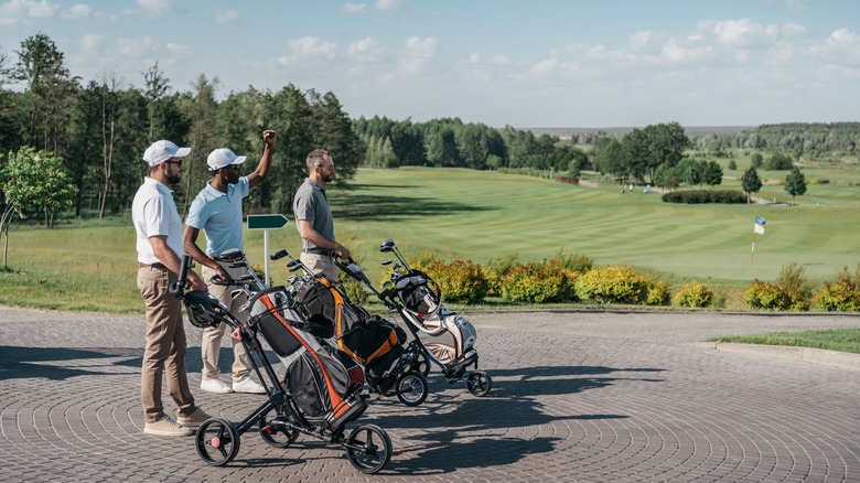 three golfers with golf club push carts looking out over green golf course