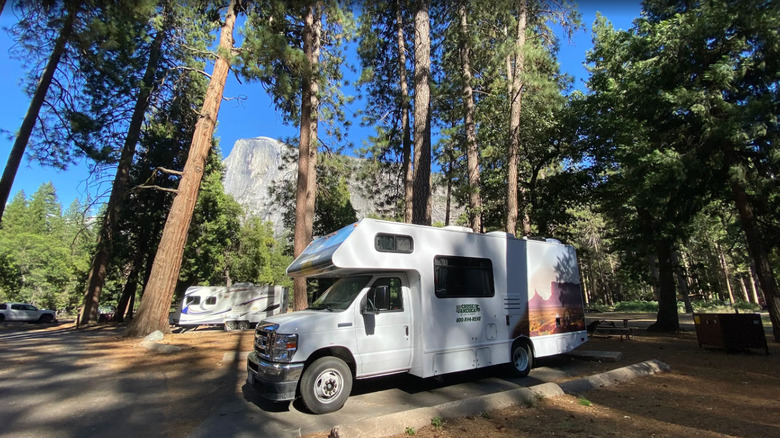 RV parked in the forest at Lower Pines Campground with view of Half Dome behind it