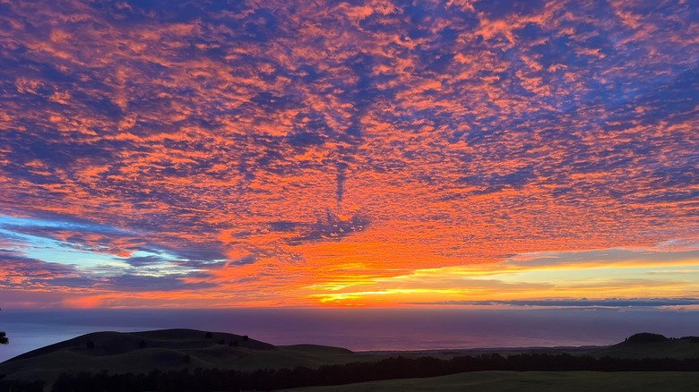 A purple, orange, yellow and blue sunset over Kāhua Ranch above Waimea