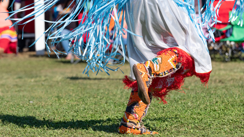 The legs of an Indigenous dancer wearing fringe and beaded moccasin shoes