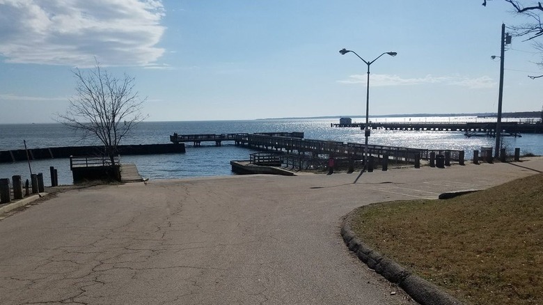 Fishing pier at Fort Armistead Park, with a driveway in the foreground, a lamp post and leafless tree beside the pier, and blue water in the background, under a blue sky