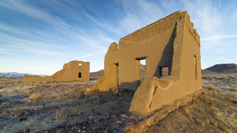 An abandoned adobe structure partially intact with blue sky and clouds overhead