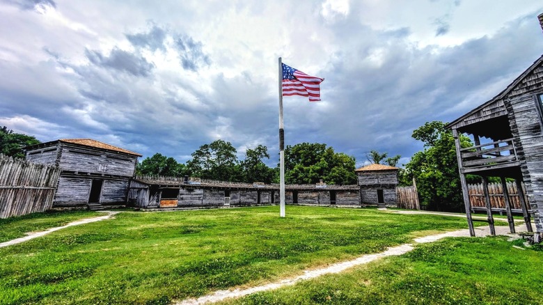 Wooden frontier fort buildings surround a green space with an American flag in the middle at Fort Osage National Historic Site