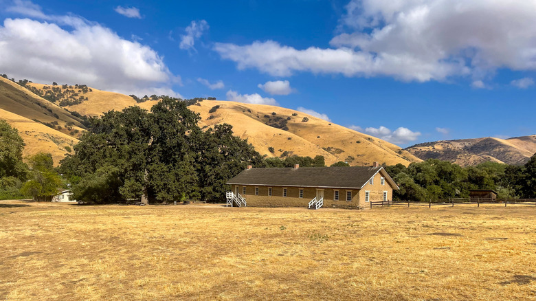 The reconstructed army barracks at Fort Tejon State Historic Park surrounded by blonde grass and oaks.