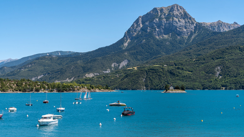 Boats on the water at Lac de Serre-Ponçon in front of verdant and soaring French Alps