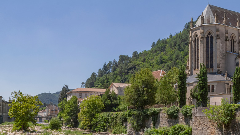 Gothic church near a rocky riverbed, with traditional houses nearby and surrounded by lush greenery, Vals-les-Bains