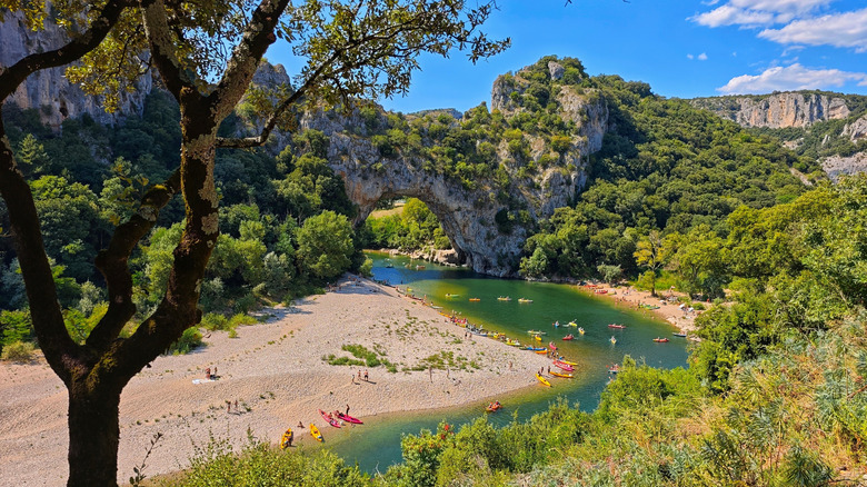 River with kayakers beneath a natural stone arch, surrounded by lush greenery near Vals-les-Bains