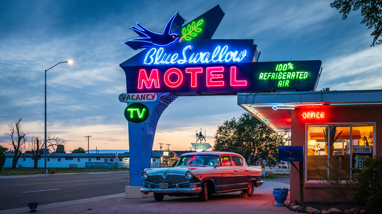 Neon sign of Blue Swallow Motel with a car parked underneath, the sky dark at sunset