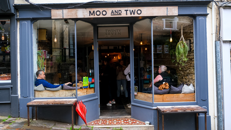 People waiting for coffee seen through the glass facade of Moo and Two, a coffee shop in Frome, England.