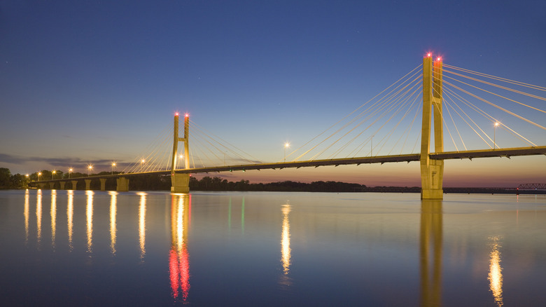 Blue water under a lit up bridge and dark blue sky in Quincy